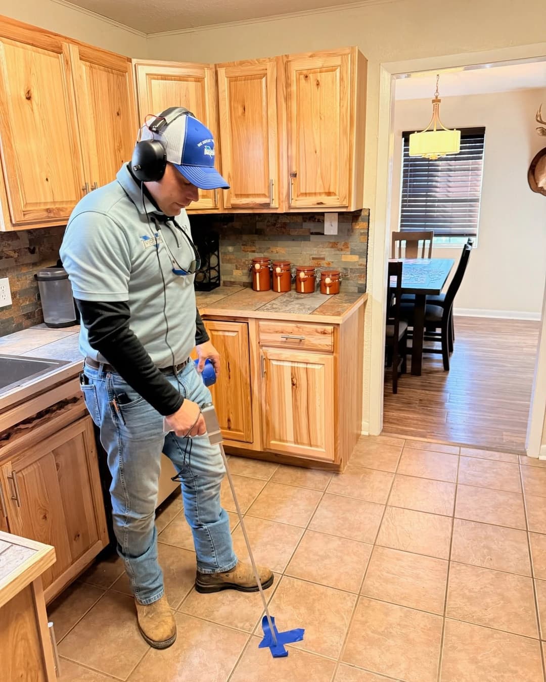A Victory plumber using an acoustic leak detector on a kitchen floor