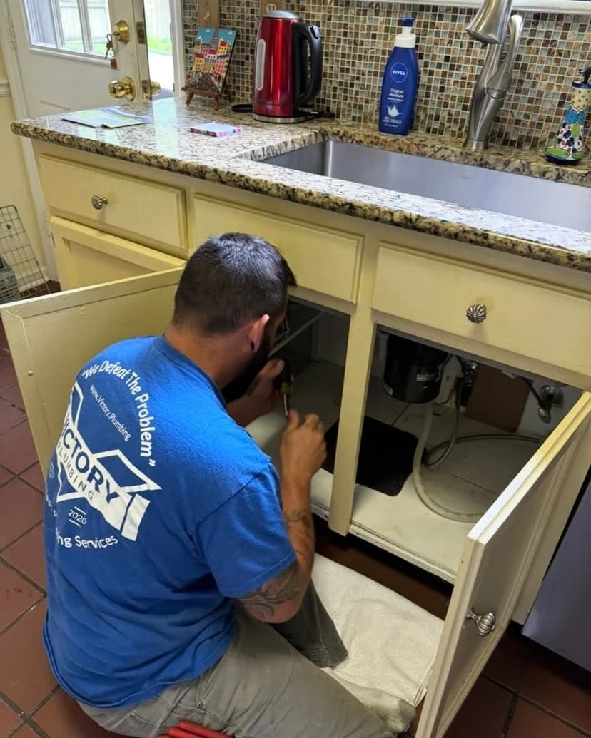 A Victory plumber working on the plumbing under a kitchen sink