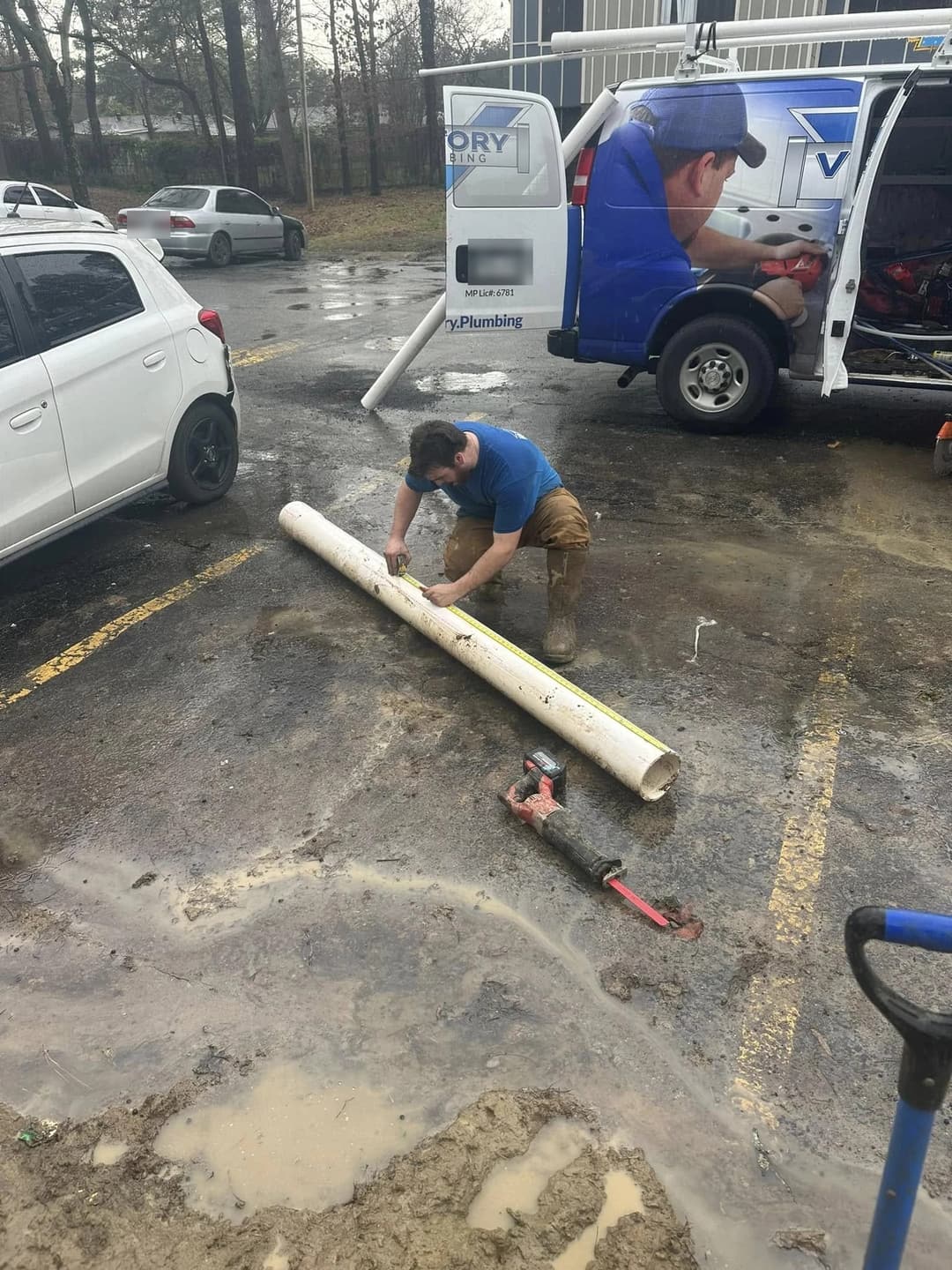 A Victory plumber measuring replacement pipe beside the branded Victory Plumbing van